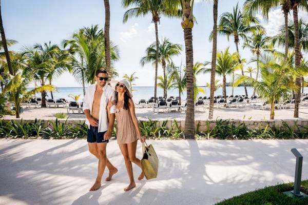 Ein Paar spaziert mit Einkaufstaschen am Barcelo Maya Beach Hotel am Strand.