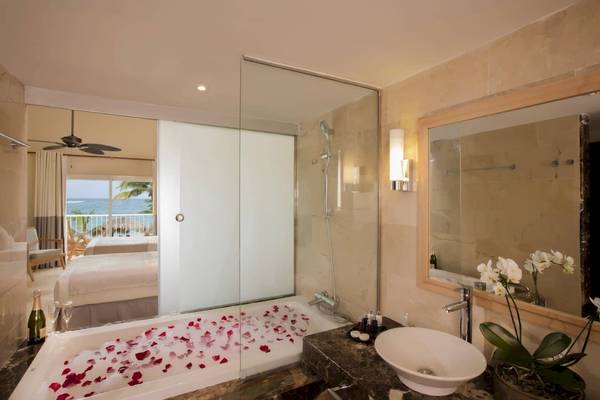 Ein Badezimmer im Grand Palladium Palace Resort & Spa mit Badewanne, Marmorboden, Spiegel, Waschbecken, und Blumen.