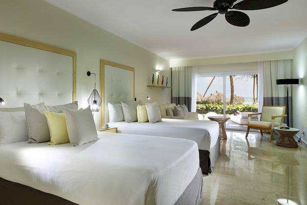 Schlafzimmer im Grand Palladium Palace Resort & Spa mit zwei Betten, Deckenventilator, Lampen und Ausblick auf Palmen.