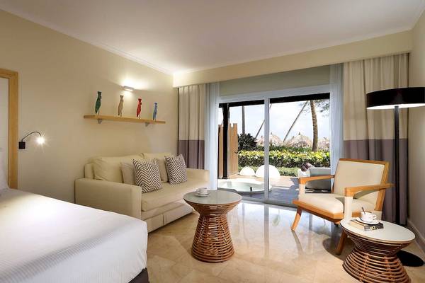 Innenansicht einer Suite im Grand Palladium Palace Resort & Spa mit einem Bett, einem Sofa, einem Tisch und einem Fenster.