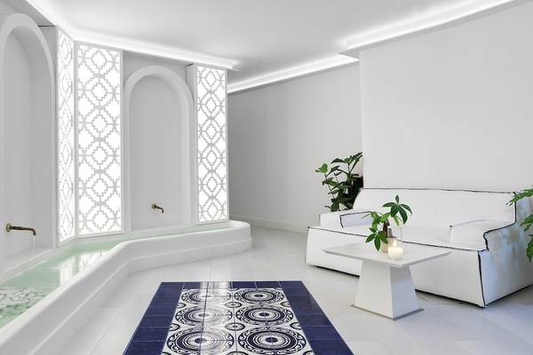 Innenansicht des Katikies Villas Mykonos mit Loungebereich, weißem Möbeln, blauem Teppich und Pflanzen.