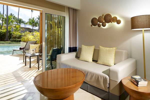 Innenraum des Grand Palladium Palace Resort & Spa mit einem Sofa, Tisch, Lampe und Blick auf den Pool.