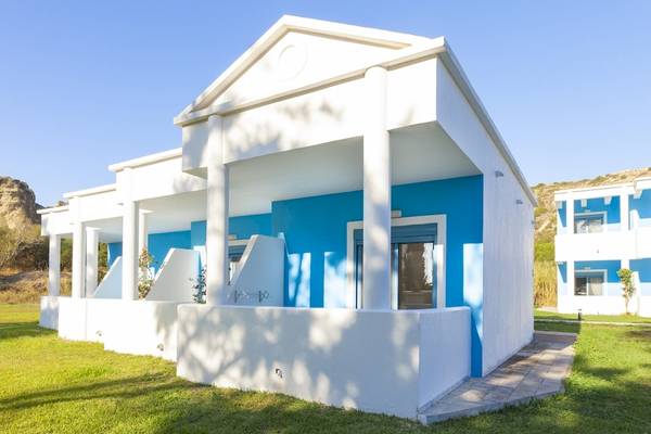 Außenansicht des Blue Sea Beach Resorts mit weißen und blauen Wänden und grüner Rasenfläche.