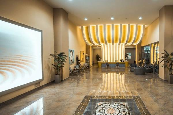 Ein Hotelfoyer mit einer großen Empfangshalle, gelben Leuchten und Pflanzen.
