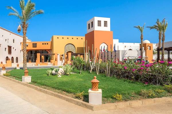 Außenansicht des PickAlbatros Oasis Port Ghalib Hotels mit Gebäuden, Palmen und einem gepflegten Rasen.