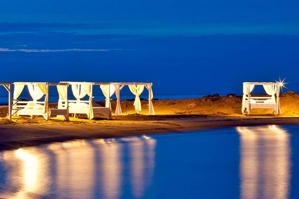Drei Betten mit Vorhängen am Strand des Knossos Beach Bungalows Suites Resort & Spa bei Nacht