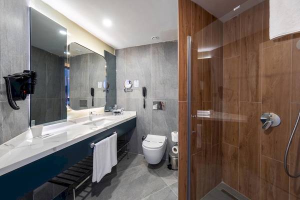 Badezimmer im Lago Hotel mit Marmorfliesen, blauer Waschtisch, Spiegel, Toilette und Duschkabine.
