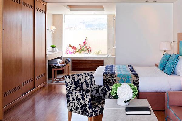 Innenansicht eines Hotelzimmers im Knossos Beach Bungalows Suites Resort & Spa mit Bett, Sessel, Tisch und Fenster.