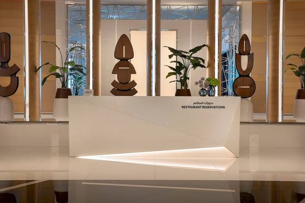 Restaurantreservierungstresen im Marriott Resort Palm Jumeirah, Dubai, mit Pflanzen und modernen Skulpturen im Hintergrund.