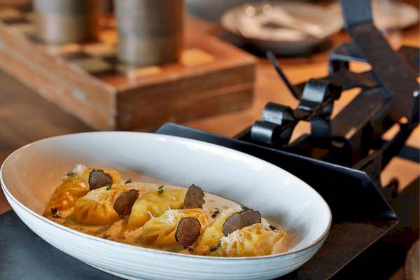 Ein Gericht mit gelben Ravioli und Trüffel in einer weißen Schüssel auf einem Tisch.