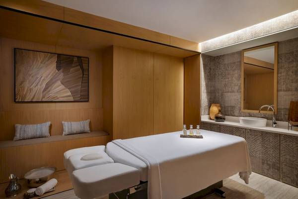Massageraum im Marriott Resort Palm Jumeirah, Dubai mit Behandlungstisch, Stühle, Holzelemente und ein Spiegel.
