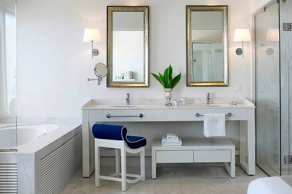 Ein Badezimmer mit einem Doppelspiegel, einer Badewanne, einem Stuhl und einer Dusche.