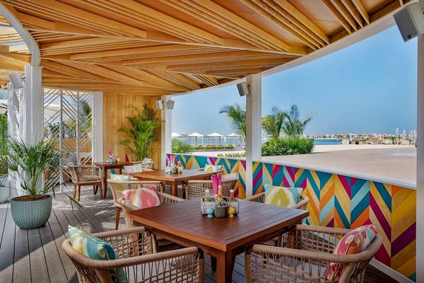 Terrasse des Marriott Resort Palm Jumeirah mit Blick auf das Meer, bunte Wände, Holztische und Stühle.