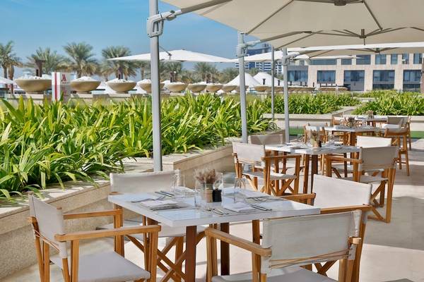 Außenbereich des Marriott Resort Palm Jumeirah in Dubai mit Tischen und Stühlen unter Sonnenschirmen.