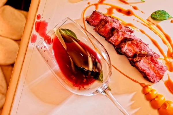 Ein Gericht mit Steak auf einem Teller, dazu ein Glas Wein, serviert im Knossos Beach Bungalows Suites Resort & Spa.