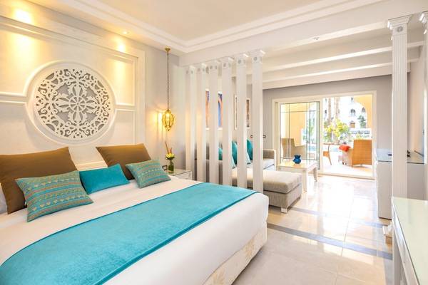 Innenansicht des Schlafzimmers im Grand Palace Hotel mit einem großen Bett, Dekor und Zugang zur Terrasse.