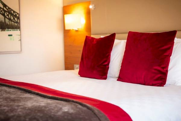Hotelzimmer im Tower Hotel, London mit rotem Kissen, weißem Bettlaken und Decken, Lampen und Gemälde an der Wand.
