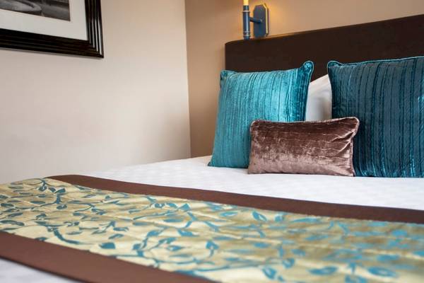 Das Bett im Tower Hotel London mit blauen und braunen Kissen und einer Wand dahinter.
