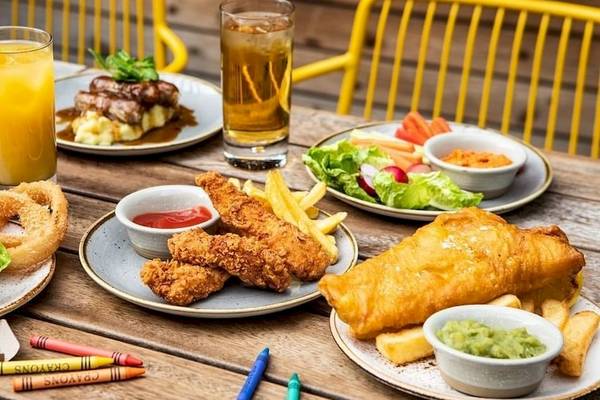 Essen und Getränke auf einem Holztisch im Tower Hotel, London. Darunter verschiedene Gerichte, Burger, Pommes, Salat und Getränke.