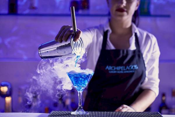 Barkeeper im Archipelagos Hotel gießt blauen Cocktail mit Raucheffekt in ein Glas.