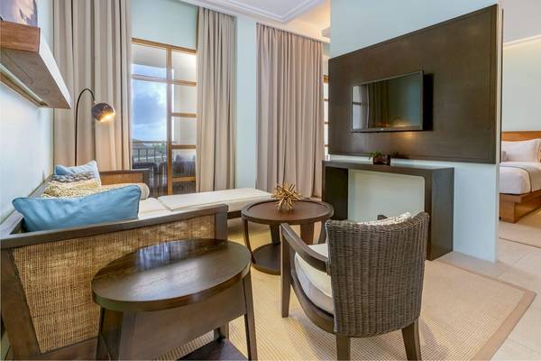 Innenansicht eines Hotelzimmers im Savoy Seychelles Resort & Spa mit Wohnzimmerbereich, Bett und Fernseher.