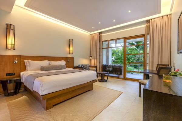 Innenansicht eines Hotelzimmers im Savoy Seychelles Resort & Spa mit einem großen Bett und einem Balkon.