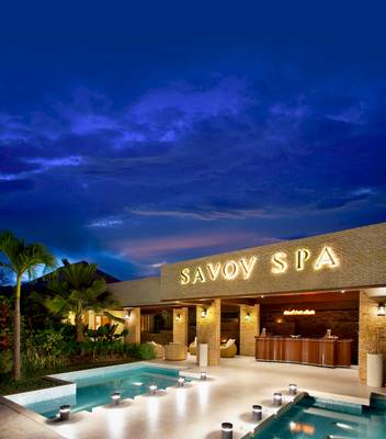 Außenansicht des Savoy Seychelles Resort & Spa bei Nacht, mit beleuchtetem Logo, Pool und Empfangstresen.