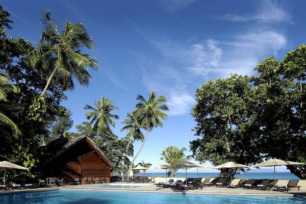 Außenbereich des Berjaya Beau Vallon Bay Resort & Casino mit Pool, Liegestühlen und Sonnenschirmen.