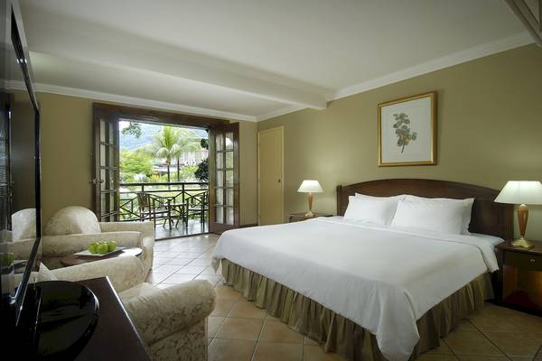 Hotelzimmer im Berjaya Beau Vallon Bay Resort & Casino mit Balkon, zwei Betten und Wohnzimmermöbeln.