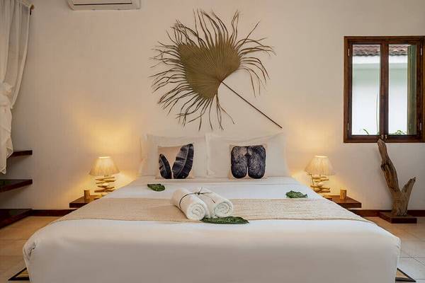 Doppelbettzimmer im Bliss Hotel Praslin mit tropischen Dekor, zwei Lampen und einem Fenster.
