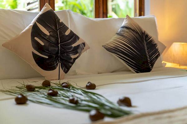 Ein Bett mit weißen Kissen und Blättern und Eicheln auf der Bettdecke im Bliss Hotel Praslin.