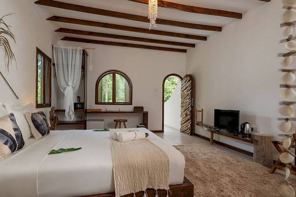 Innenansicht eines Schlafzimmers im Bliss Hotel Praslin mit Bett, Fernseher und offenem Fenster.