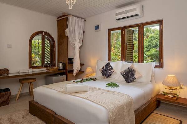 Schlafzimmer im Bliss Hotel Praslin mit großem Bett, Klimaanlage und Fenstern zur Außenseite.