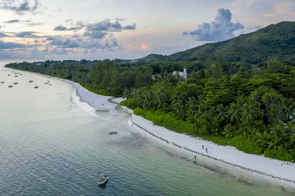 Luftaufnahme des Bliss Hotel Praslin mit Strand, Bäumen und Berg im Hintergrund.