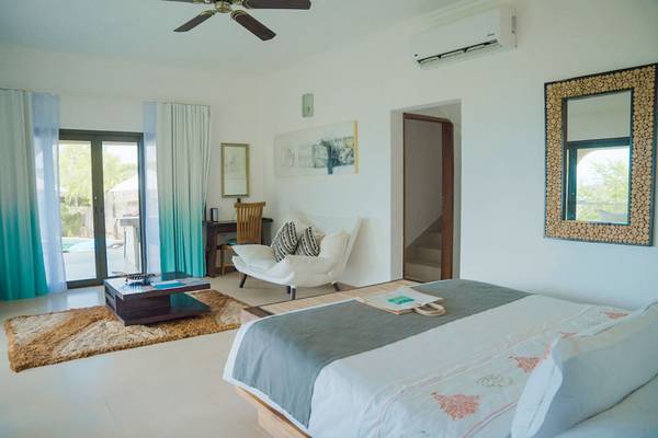 Schlafzimmer im Le Duc de Praslin Hotel & Villas mit Bett, Chaiselongue, Tisch und Klimaanlage.