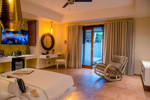 Schlafzimmer im Le Duc de Praslin Hotel & Villas mit Bett, Fernseher, Schreibtisch und Sessel.