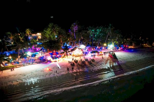 Le Duc de Praslin Hotel & Villas bei Nacht mit bunten Lichtern und Menschen auf dem Strand.