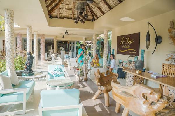 Lobbybereich des Le Duc de Praslin Hotel & Villas mit zwei Frauen und einem Mann, die sich unterhalten.