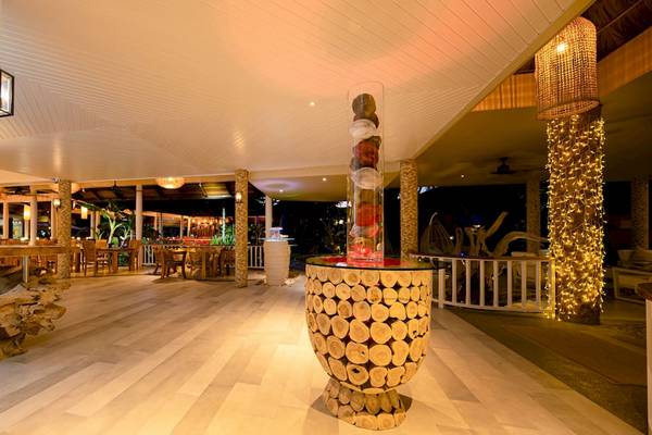 Innenbereich des Le Duc de Praslin Hotel & Villas mit hölzerne Struktur, leuchtenden Lampen und Tischen.