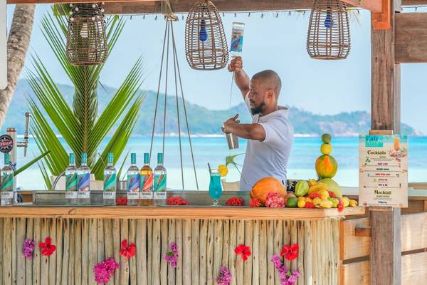 Ein Mann, der Cocktails an einer Strandbar zubereitet, mit Früchten und Deko im Hintergrund.