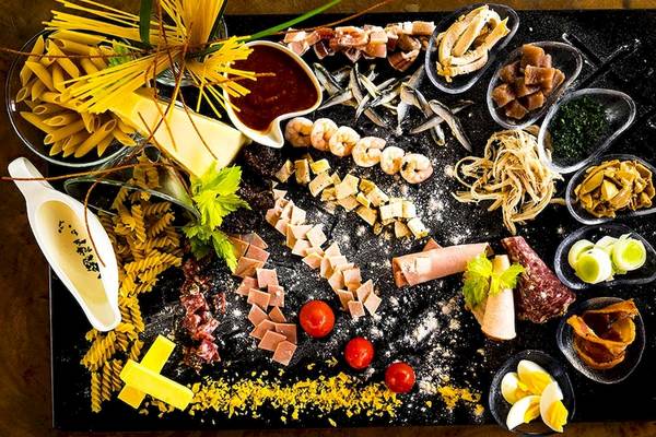 Frühstücksbuffet mit Pasta, Fisch, Schinken und Gemüse auf einem schwarzen Teller.