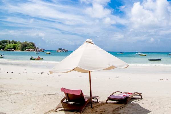 Strand mit Sonnenschirm und Liegen im Hintergrund befindet sich ein Hotel