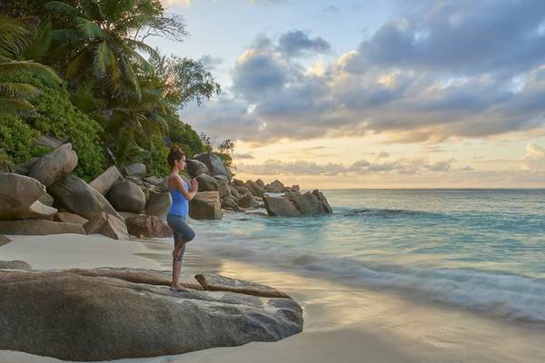 Frau praktiziert Yoga auf einem Felsen am Strand im Constance Lemuria Seychelles