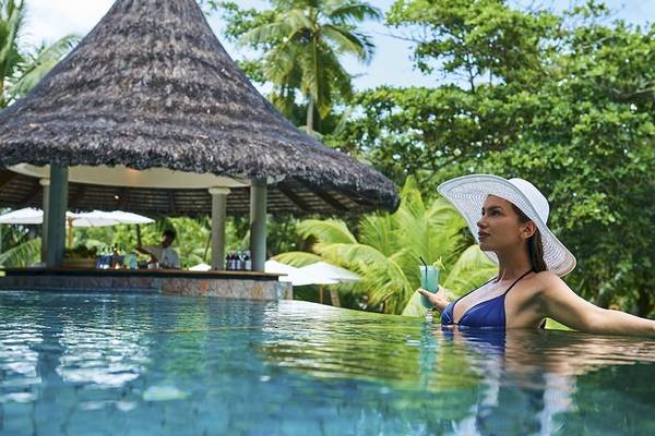 Eine Frau genießt einen Drink am Pool des Constance Lemuria Seychelles