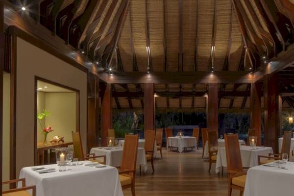 Innenbereich des Restaurants im Anantara Maia Seychelles Villas mit gedeckten Tischen und dekorativen Kerzen.