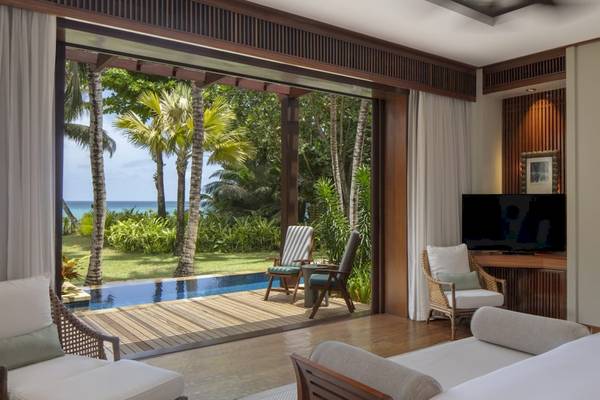 Innenansicht des Schlafzimmers im Anantara Maia Seychelles Villas mit Blick auf einen Pool und einen Garten.