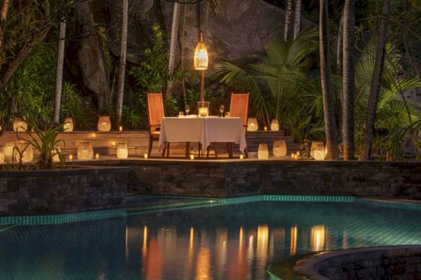 Pool-Dinnertisch im Anantara Maia Seychelles Villas bei Nacht mit illuminierten Laternen.