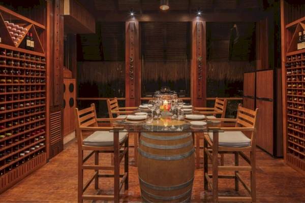 Weinkeller des Anantara Maia Seychelles Villas mit runden Tisch, Weinflaschen und Holzregalen