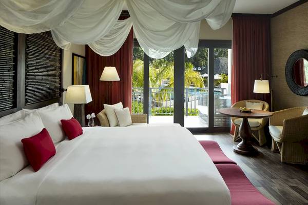 Ein elegantes Schlafzimmer im STORY Seychelles Hotel mit einem großen Bett, roten Kissen, und einem Ausblick auf den Pool.