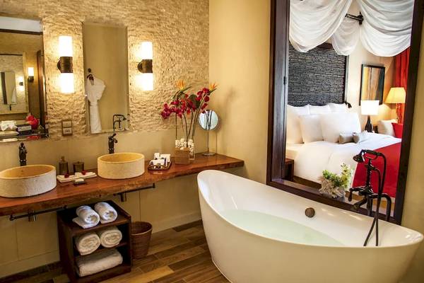 Ein Badezimmer im STORY Seychelles Hotel mit zwei Waschbecken und einer Badewanne, die das Schlafzimmer widerspiegelt.